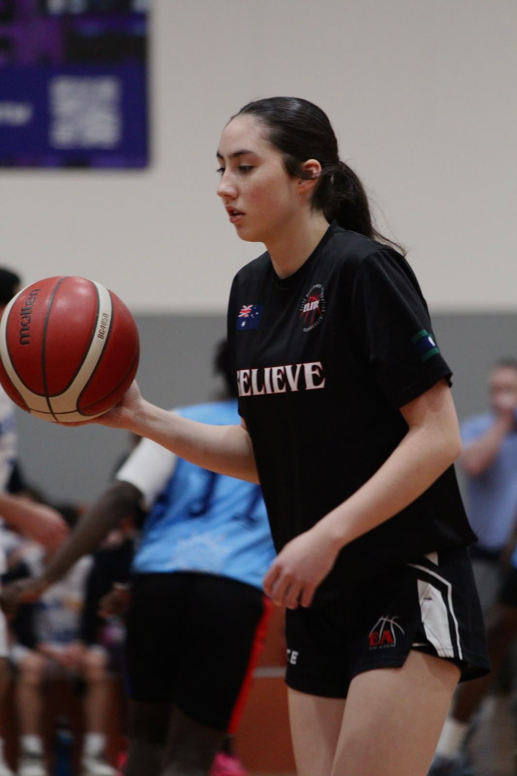 A player in an Elite Believe warm-up shirt with a ball